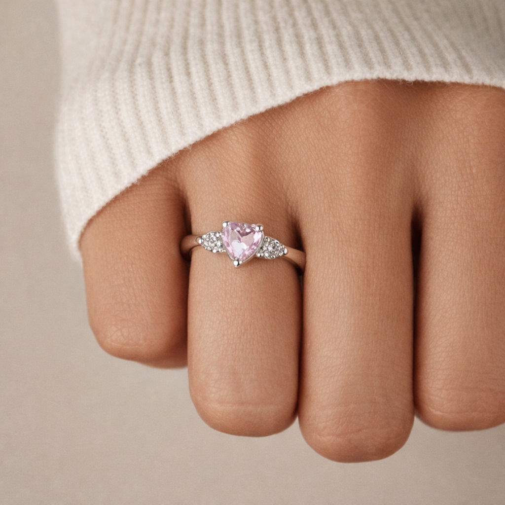 Pink heart-shaped diamond ring on a finger with a neutral background