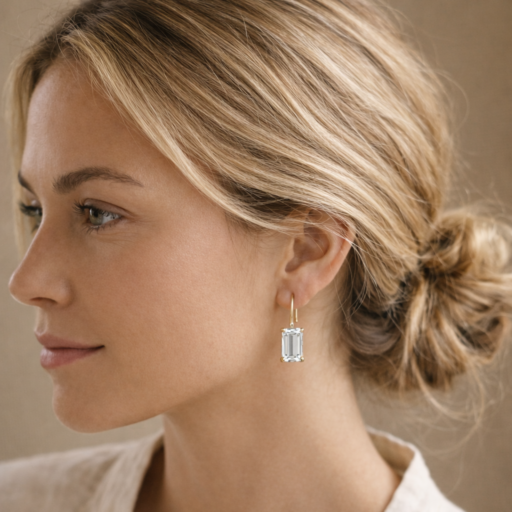 Woman wearing a gold earring with a clear gemstone against a neutral background