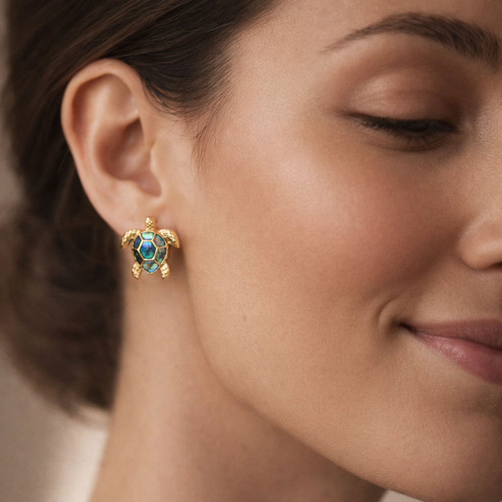 Close-up of a woman wearing gold earrings with a blue gemstone against a neutral background