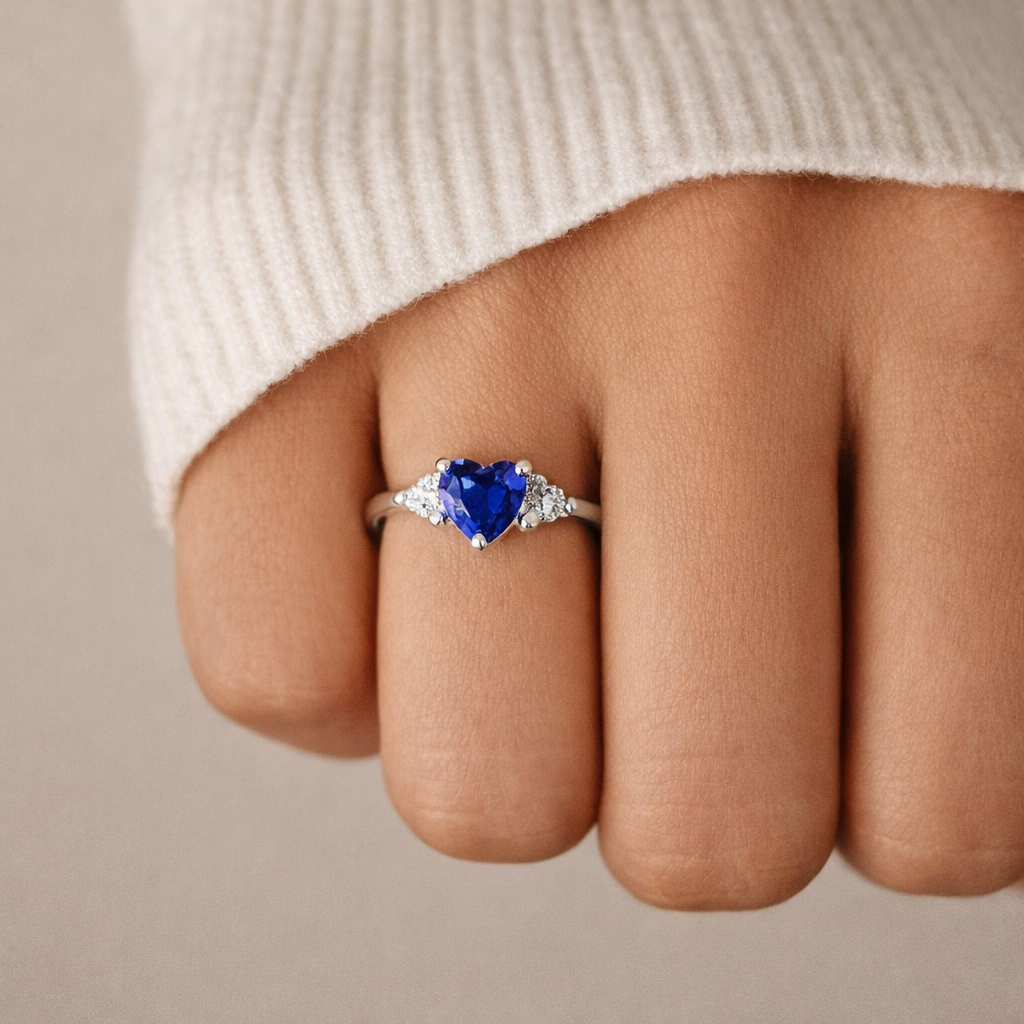 Heart-shaped blue gemstone ring on a finger with a neutral background