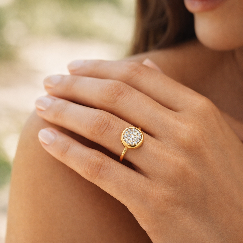 Close-up of a hand wearing a gold ring with a diamond cluster, against a blurred natural background.