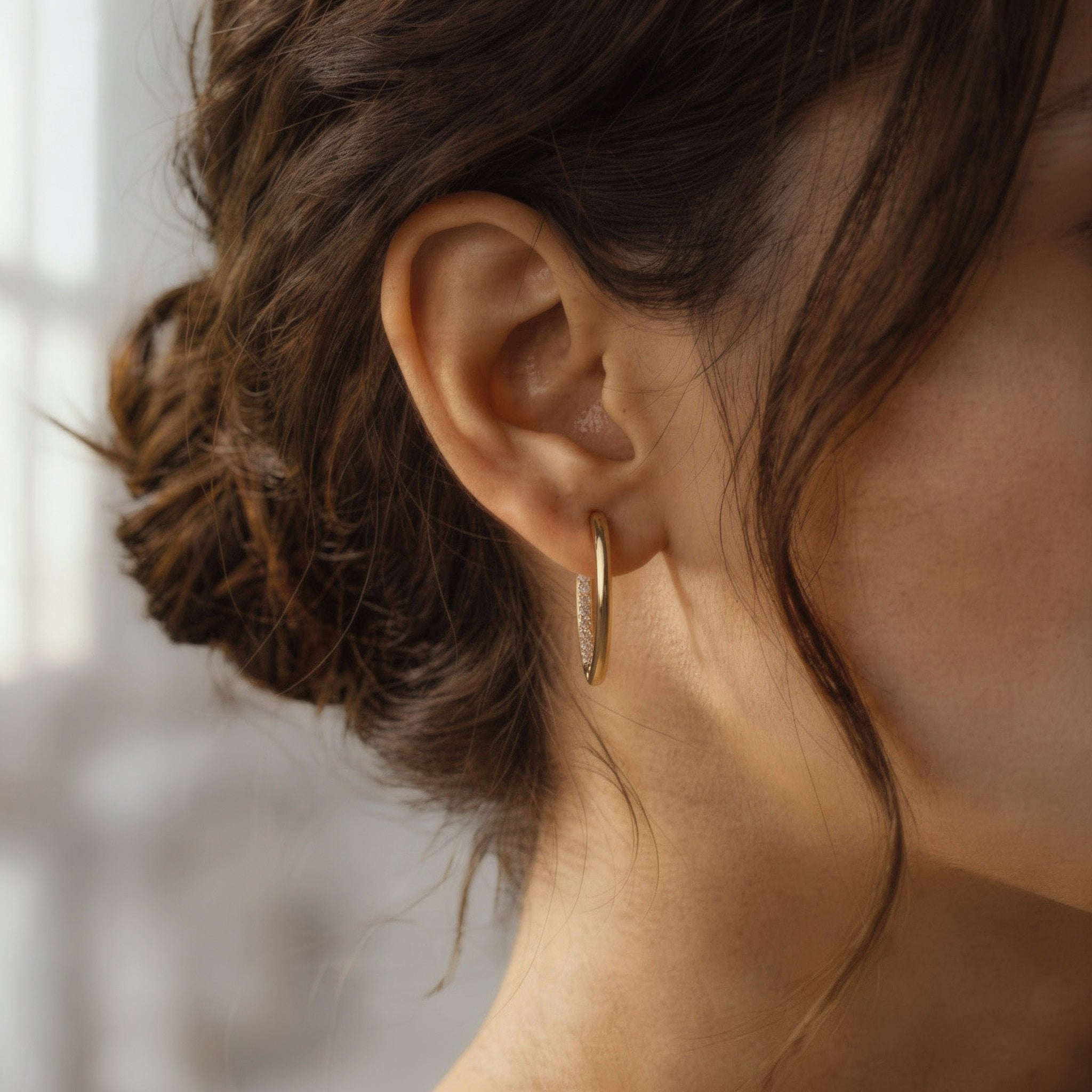 Close-up of an ear wearing a gold hoop earring with blurred background