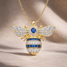 Gold bee-shaped necklace with blue gemstone on a beige background