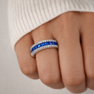 Close-up of a hand wearing a ring with blue gemstones on a neutral background