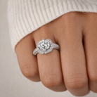 Silver ring with a diamond on a person's finger against a neutral background