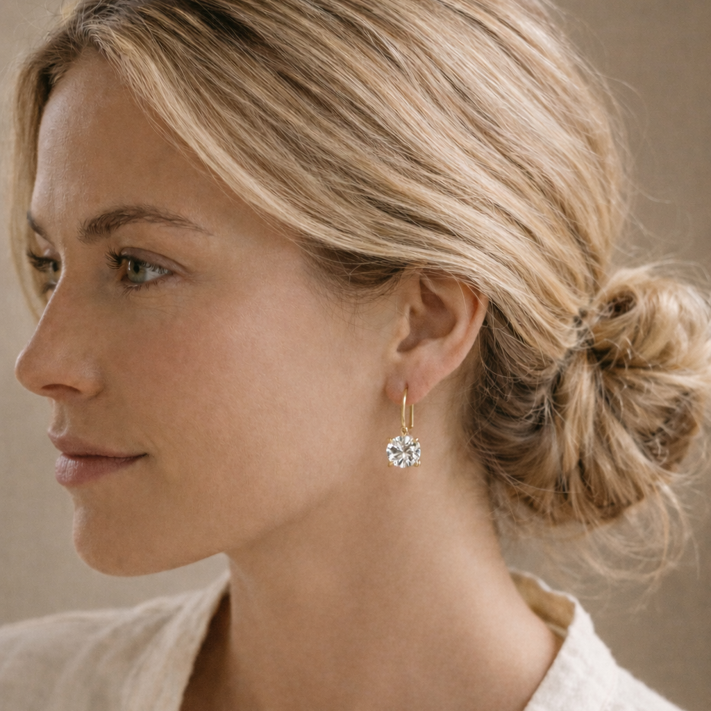 Woman wearing a gold earring with a clear gemstone against a neutral background