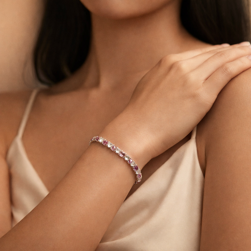 Close-up of a woman's arm wearing a bracelet with pink gemstones, against a neutral background.