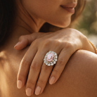 Close-up of a hand wearing an ornate ring with a pink gemstone, outdoors.