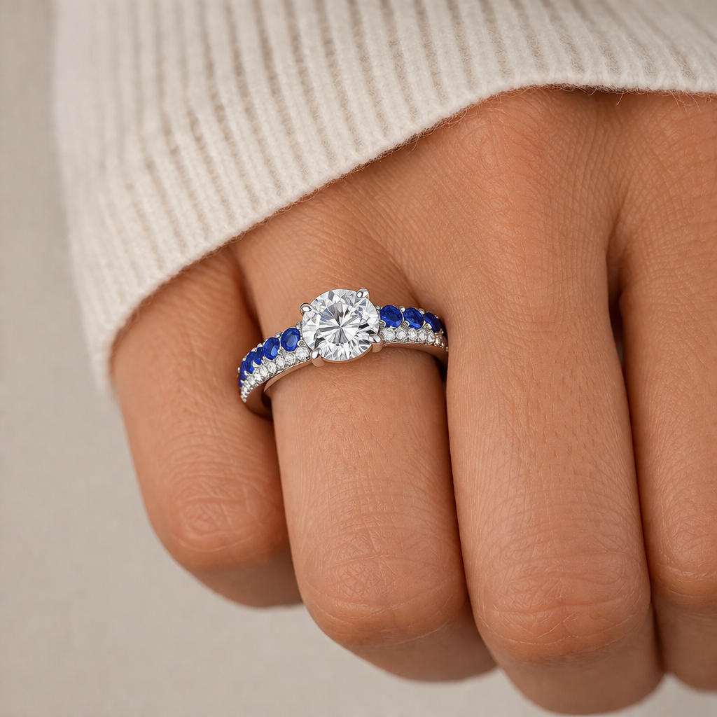 Close-up of a hand wearing a ring with a diamond and blue gemstones on a neutral background