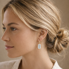 Woman wearing a gold earring with a clear gemstone against a neutral background