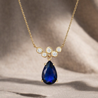 Gold necklace with a blue teardrop pendant on a neutral background